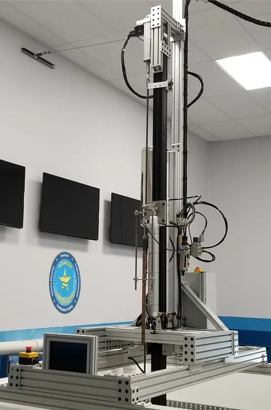 The robotic APSP-16 drain cover test rig under the lab's wall monitors